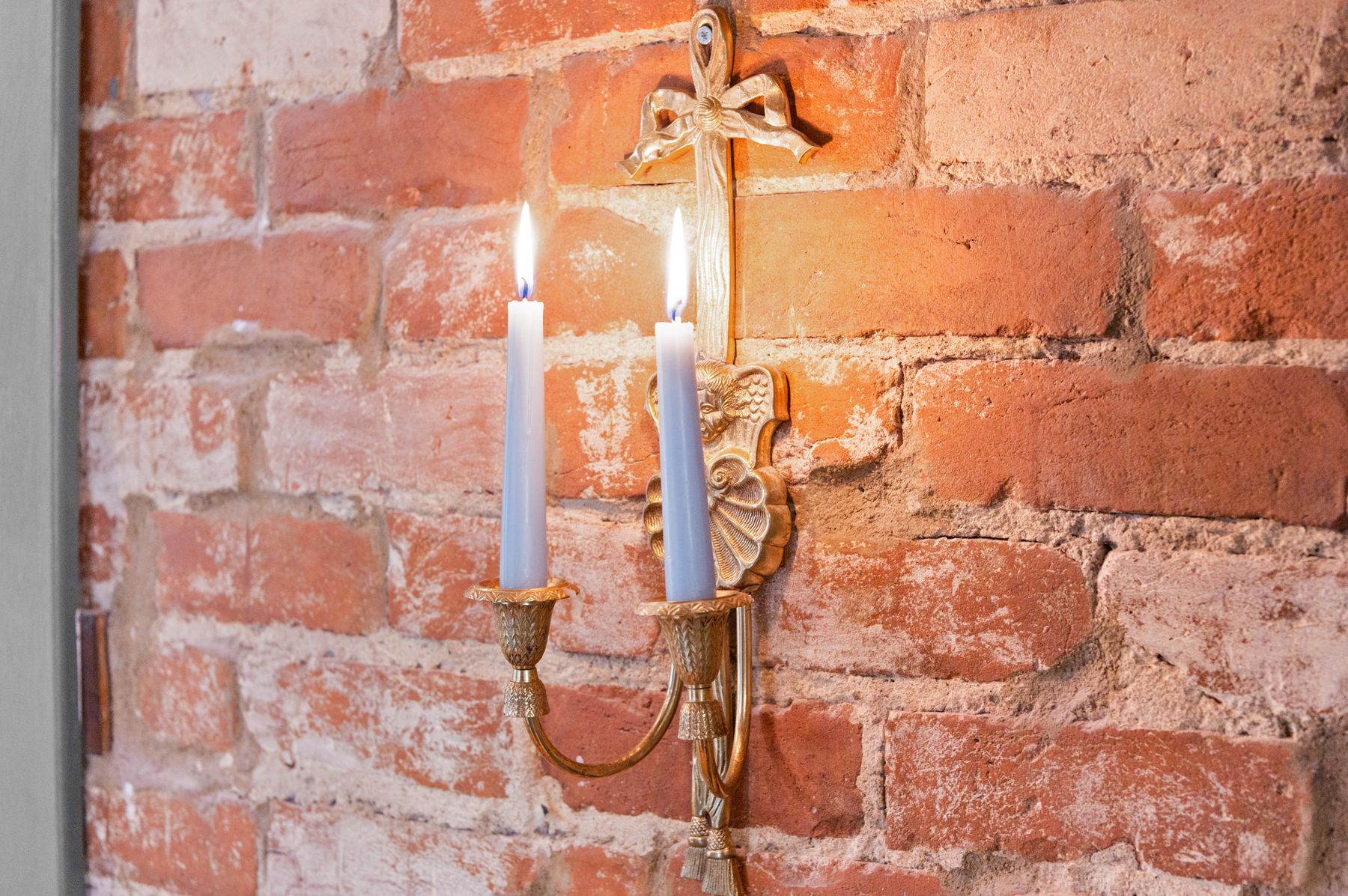 Gilt bow-and-tassel candle sconce on exposed brick